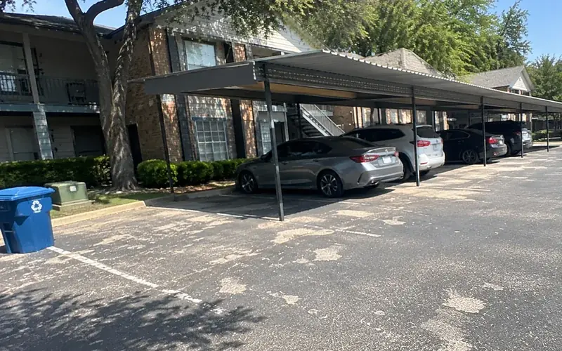 Apartment complex exterior with a metal-roof carport and asphalt lot with faded striping