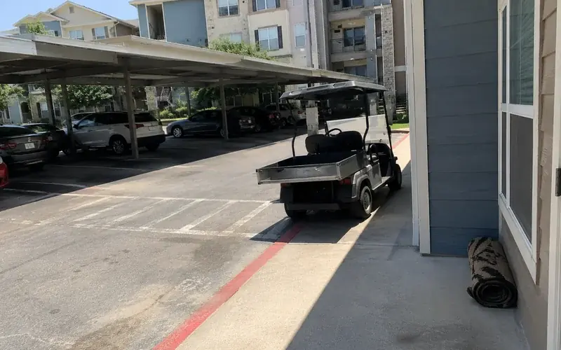 Apartment exterior with a metal-roof carport and parked cars with faded lot striping