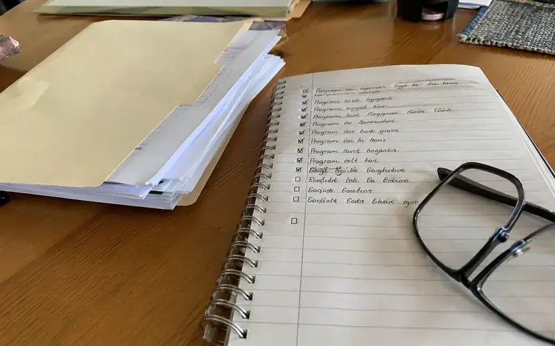Handwritten checklist of program documents beside a folder of paperwork on a desk
