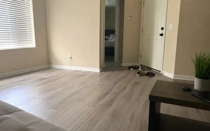 Empty apartment living room with vinyl plank flooring, white blinds, and beige walls