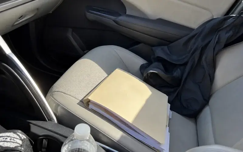 Folder of relocation paperwork on a car passenger seat with daylight through the window