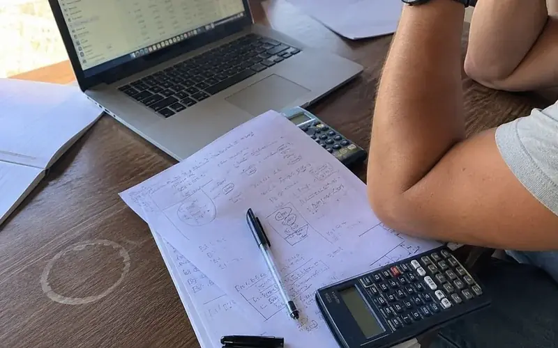 Handwritten negotiation notes and a calculator beside a laptop showing an account balance