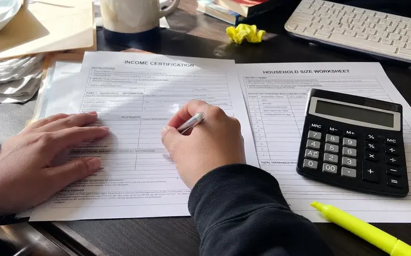 Income certification form and a household size worksheet beside a calculator