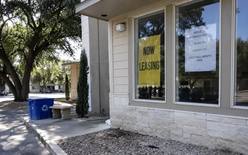 Leasing office window with a now-leasing banner and a concession flyer taped inside the glass