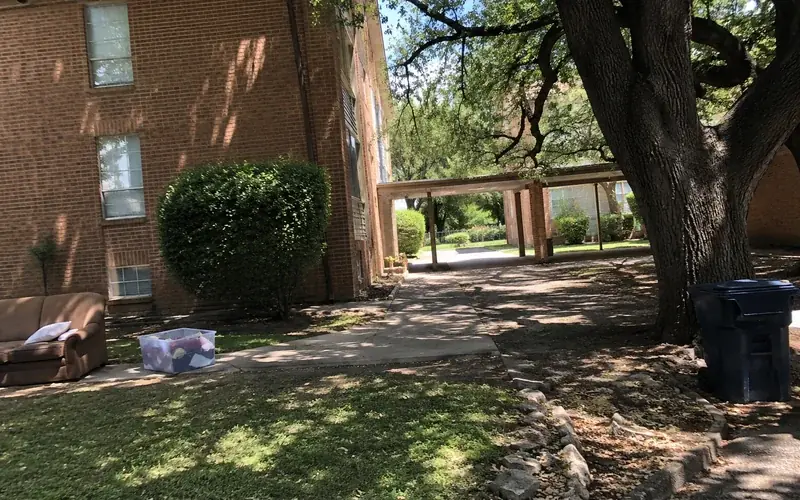 Older brick apartment building exterior with a breezeway and a mature live oak