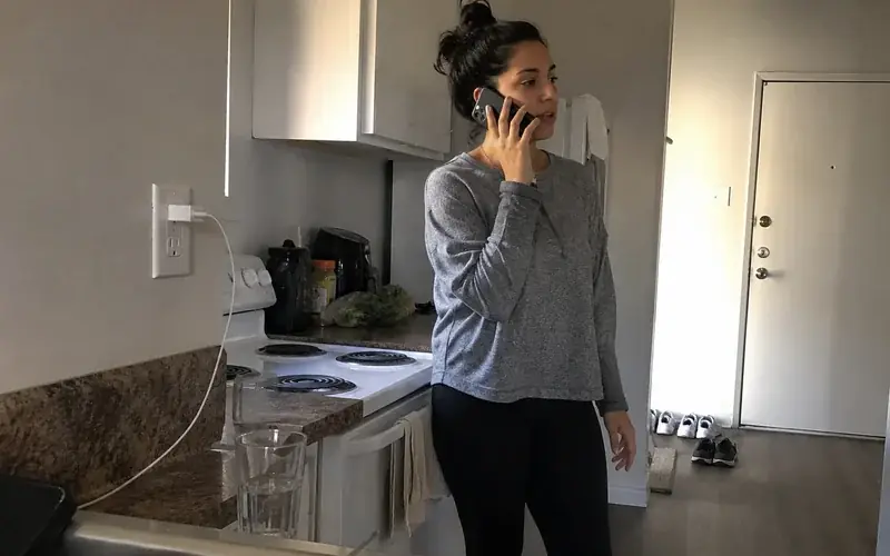 Person on a phone call in an apartment kitchen with laminate counters, unposed