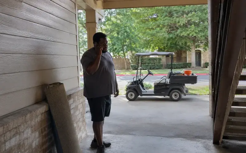 Person on a phone call standing in an apartment breezeway, casual clothing, unposed