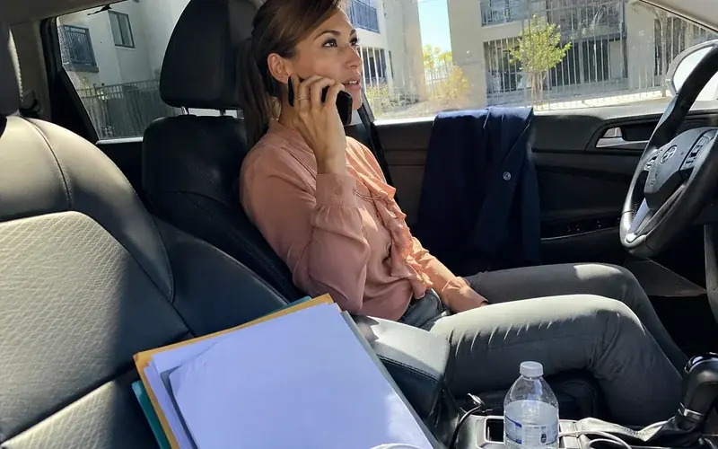 Person on a phone in a car with paperwork on the passenger seat, unposed
