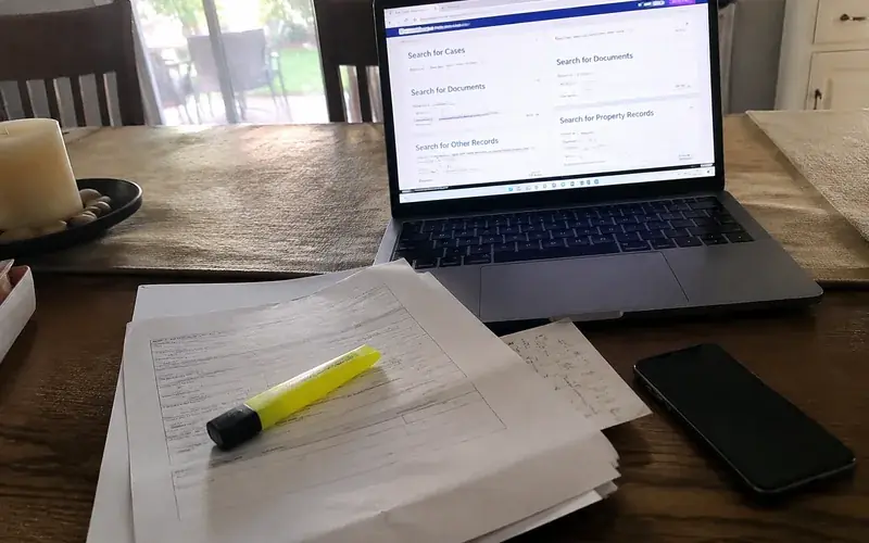 Printed court paperwork and a highlighter on a desk beside a laptop showing a records search page