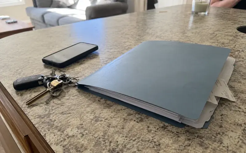 Set of keys on a laminate countertop next to a lease folder in natural daylight