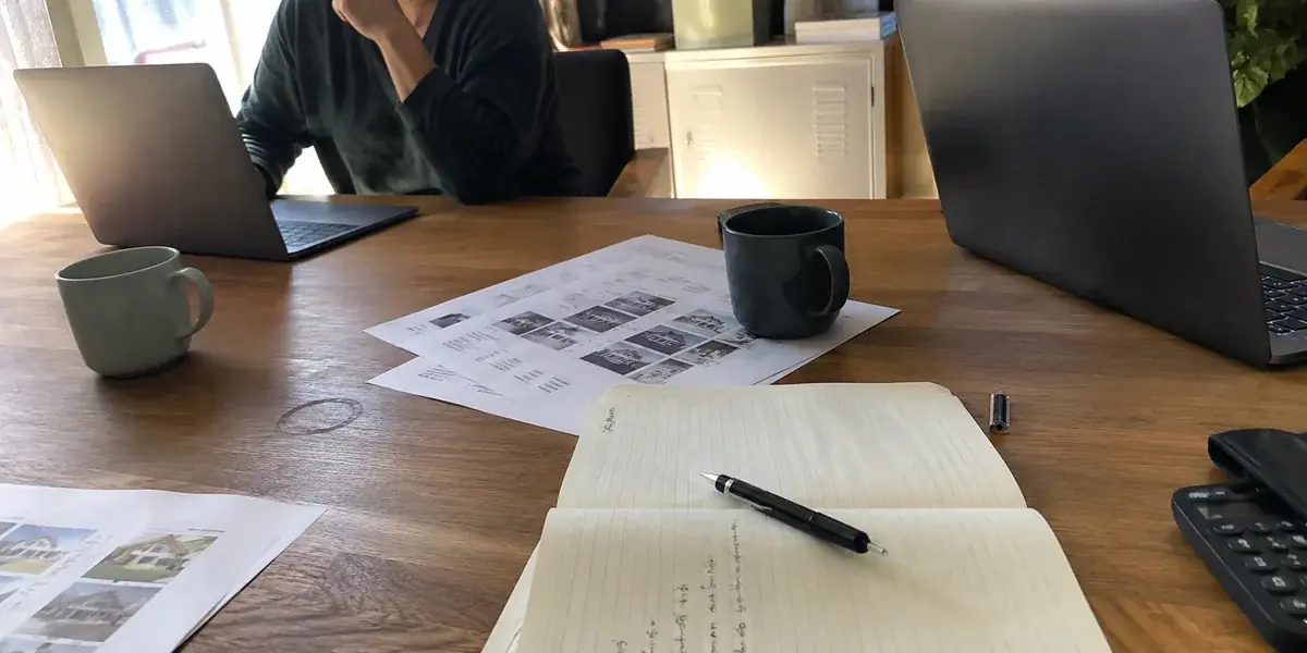 Shared office desk with laptops, printed property criteria sheets, and a notepad