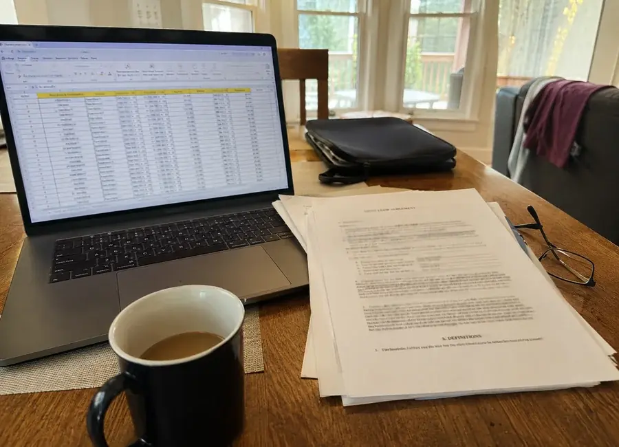 Laptop showing Tarrant County apartment criteria spreadsheet beside a printed lease agreement