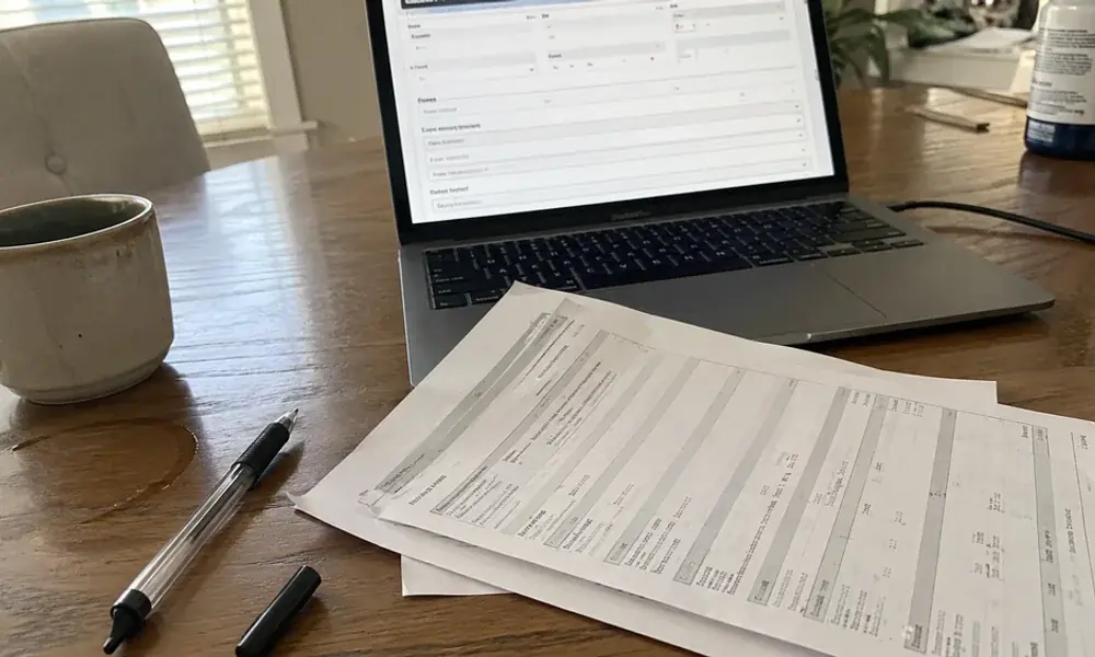Laptop showing a lease guarantee application for a Fort Worth apartment beside printed pay stubs