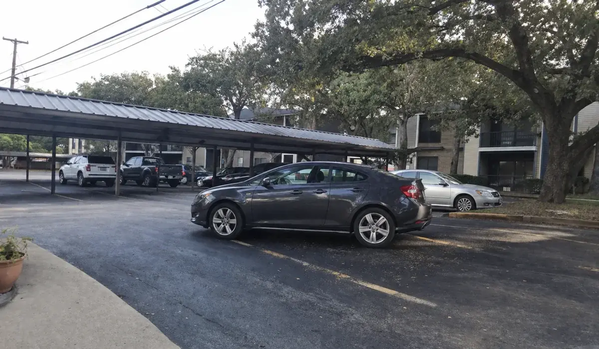 Fort Worth apartment complex near Loop 820 with metal-roof carports and live oaks under a gray sky